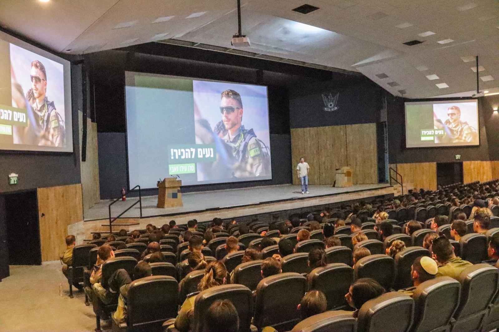 עידו זאבי מרצה באולם מלא חיילים וחיילות, ועל המסכים שקופית 'נעים להכיר'